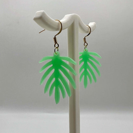 3d printed monstera earrings hanging on a display stand